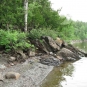 Colour photograph of beach pebbles, rocky shoreline, trees and water