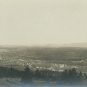 Photographie noir et blanc d’une ville au loin, entourée de champs et d’arbres
