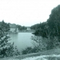 Photographie noir et blanc d’un lac et d’arbres avec un ancien bâtiment en bois