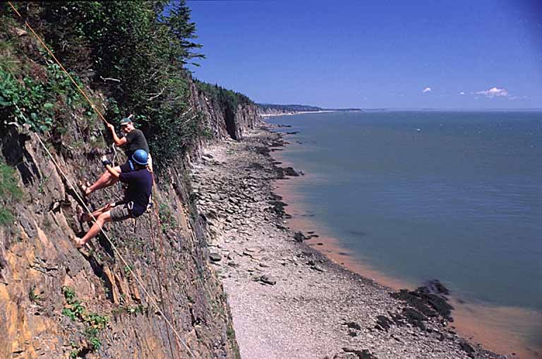 Photographie couleur d’une falaise rocheuse le long d’un rivage et de deux personnes qui pratiquent l’escalade