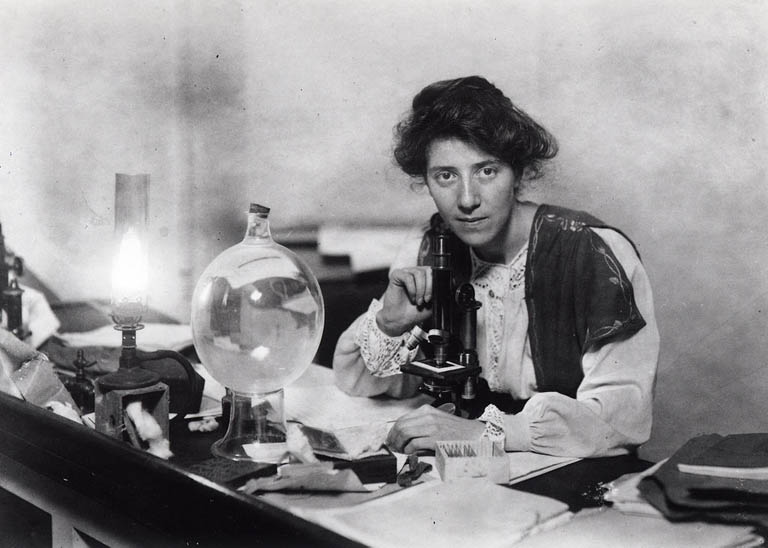 Photographie noir et blanc d’une femme assise à un microscope d’autrefois