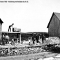 Photographie noir et blanc montrant une mine de roches, des bâtiments, des hangars, des roches et un homme sur le toit d'un hangar