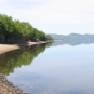 Photographie couleur d’un plan d'eau calme, d’un rivage rocailleux et d’arbres