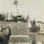 Black and white photograph of a square headstone in a cemetery with a stone pot on top