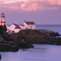 Colour photograph of rocky coastline and ocean with red and white lighthouse