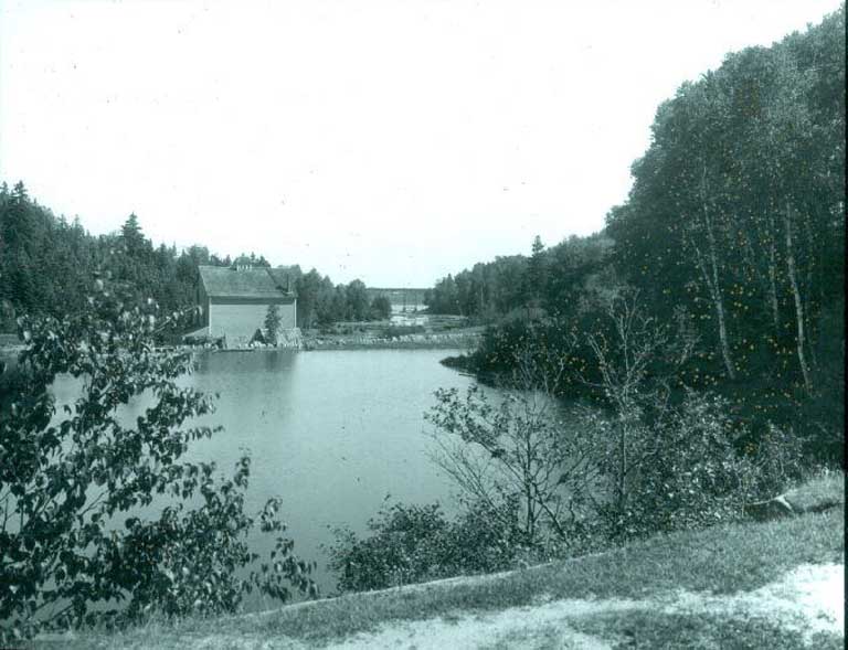 Black and white photograph of a lake and trees with and old wooden building